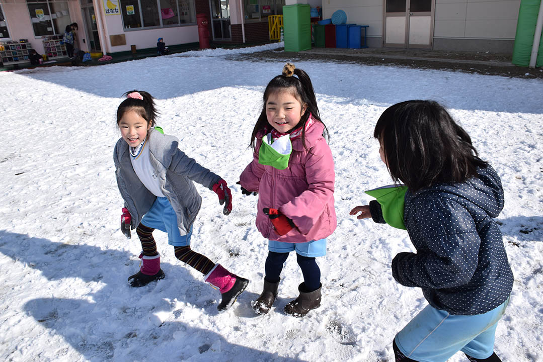 雪が積もった園庭で遊ぶ子どもたちです